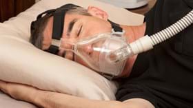 Male patient asleep on his side in bed with CPAP mask